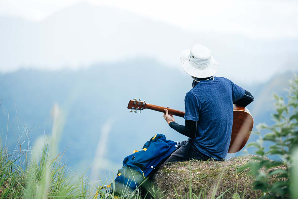 man in white hat playing guitar sitting on top of a rock